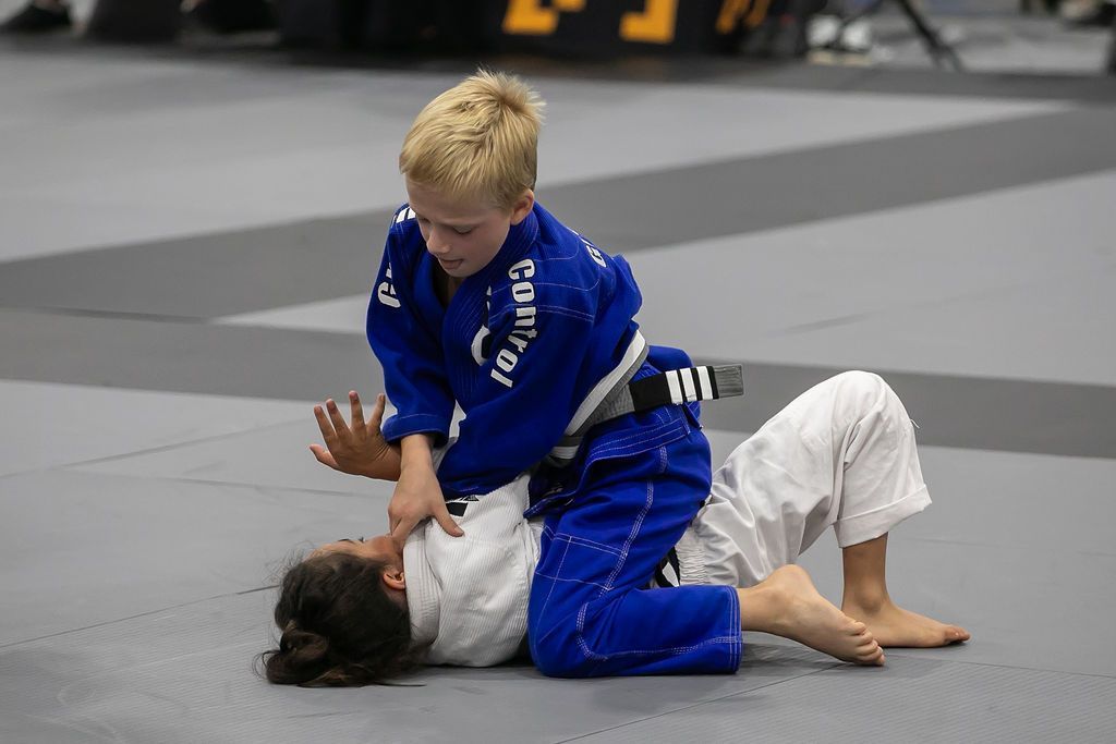 Two children in blue and white martial arts uniforms grappling on a mat