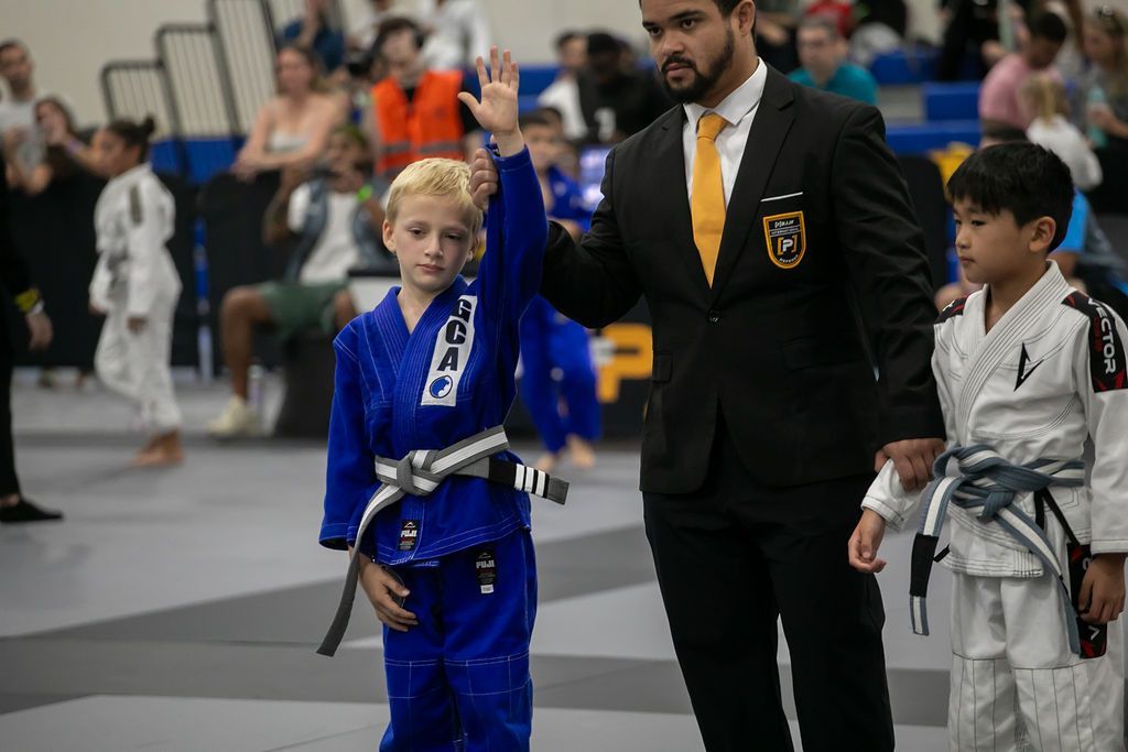 Children in martial arts uniforms standing on mats with an instructor during a class or tournament
