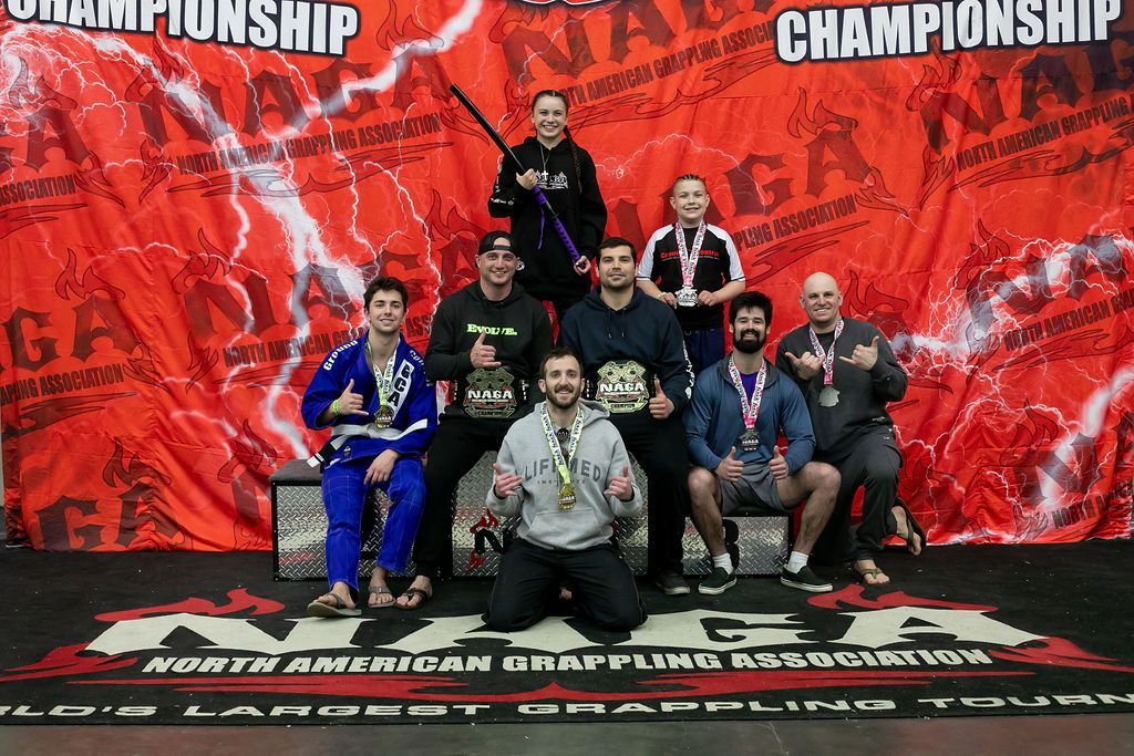 Group of martial arts competitors posing on a mat in front of a red championship backdrop