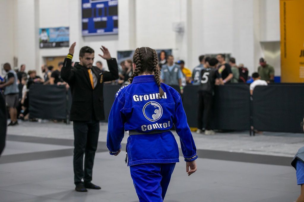 Person in blue tracksuit walking in an indoor event hall while another person waves nearby.