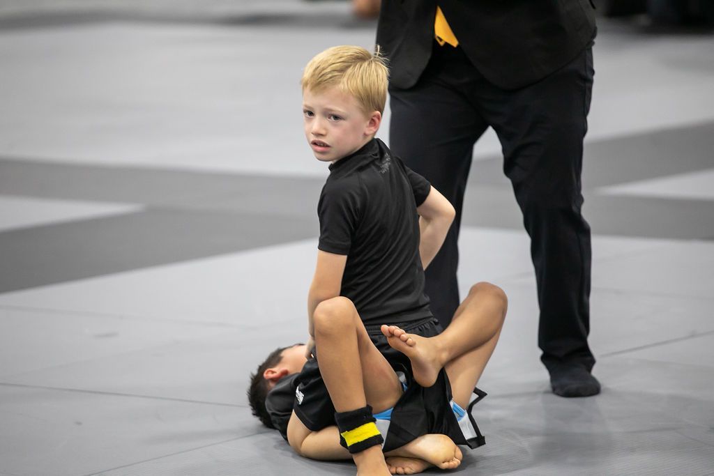 Wrestling match with one athlete pinning another on a gray mat, referee standing nearby