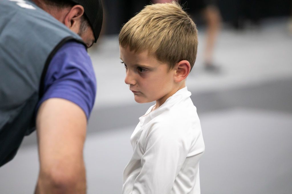 Adult leaning toward a child in a white shirt, both focused in a gray indoor setting