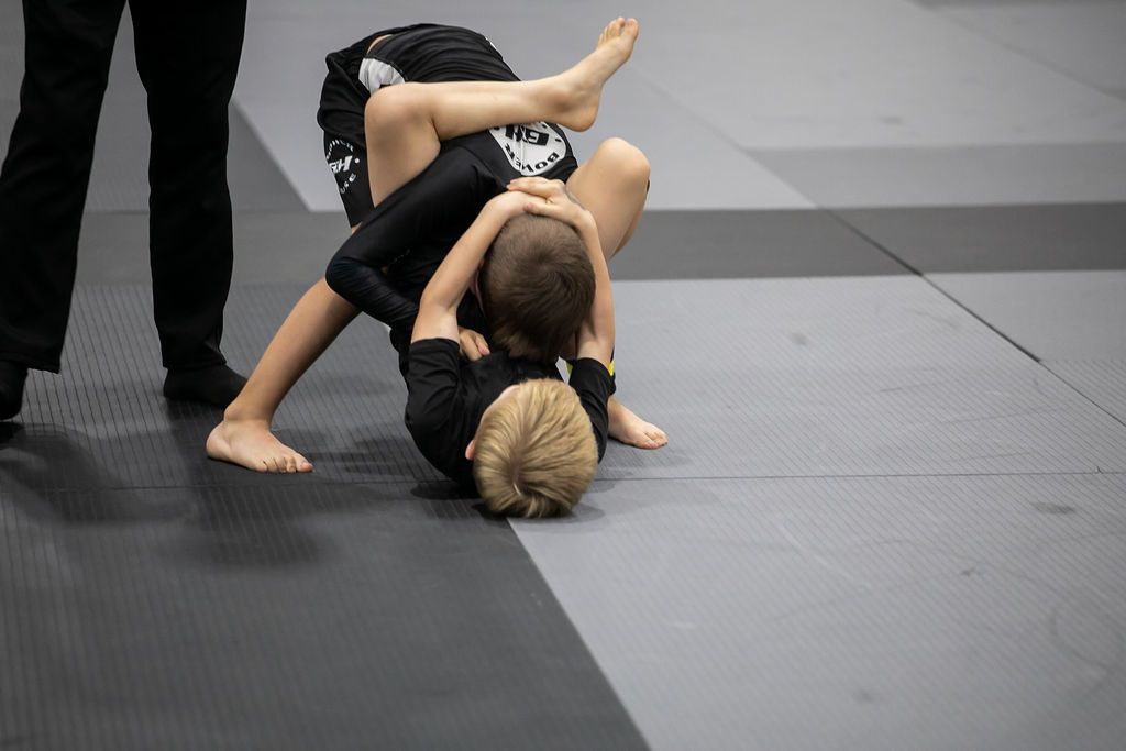 Two children grapple on a mat during a martial arts practice or competition.