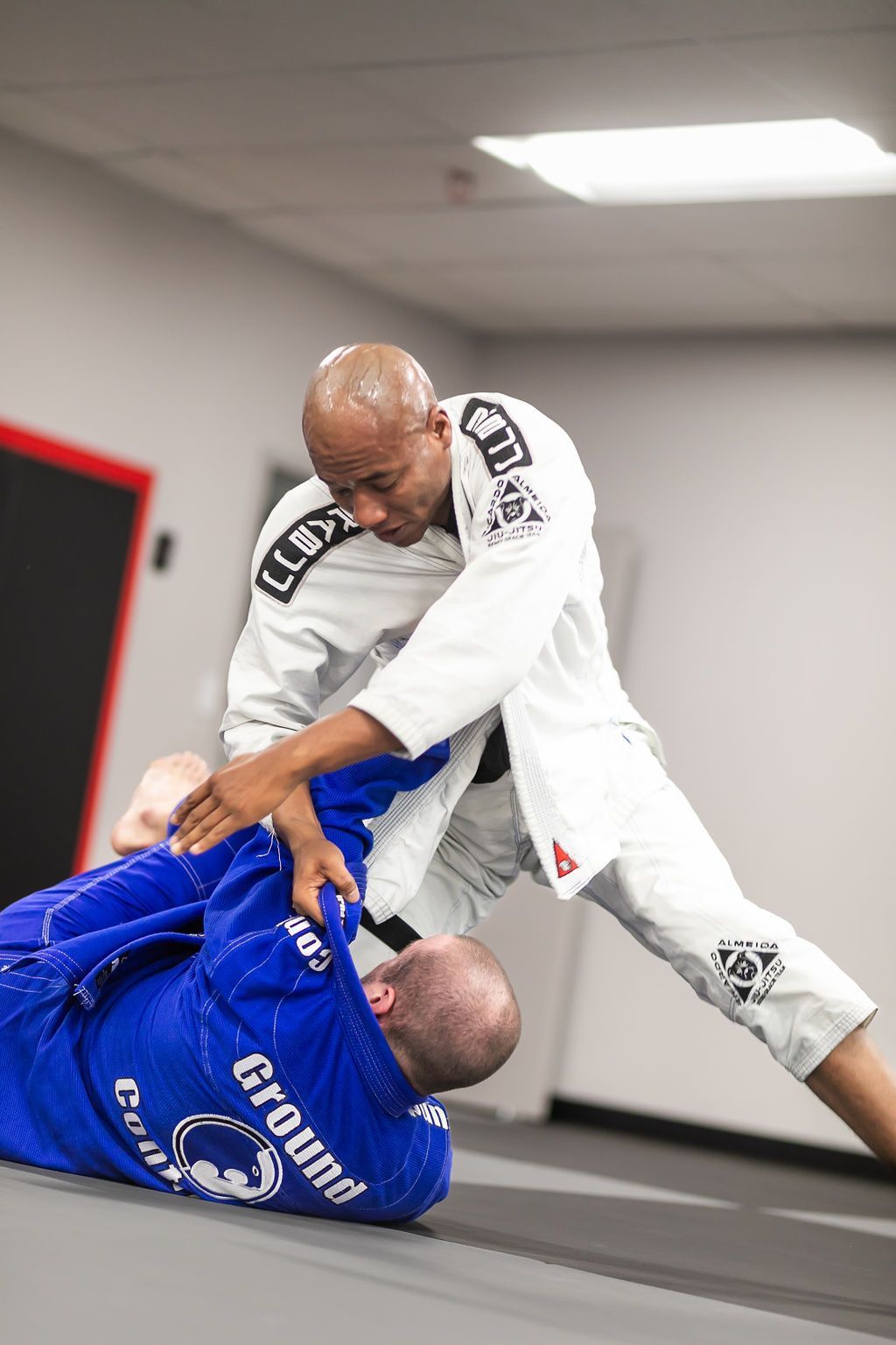 Two martial artists grappling on a mat, one in white controlling one in blue.