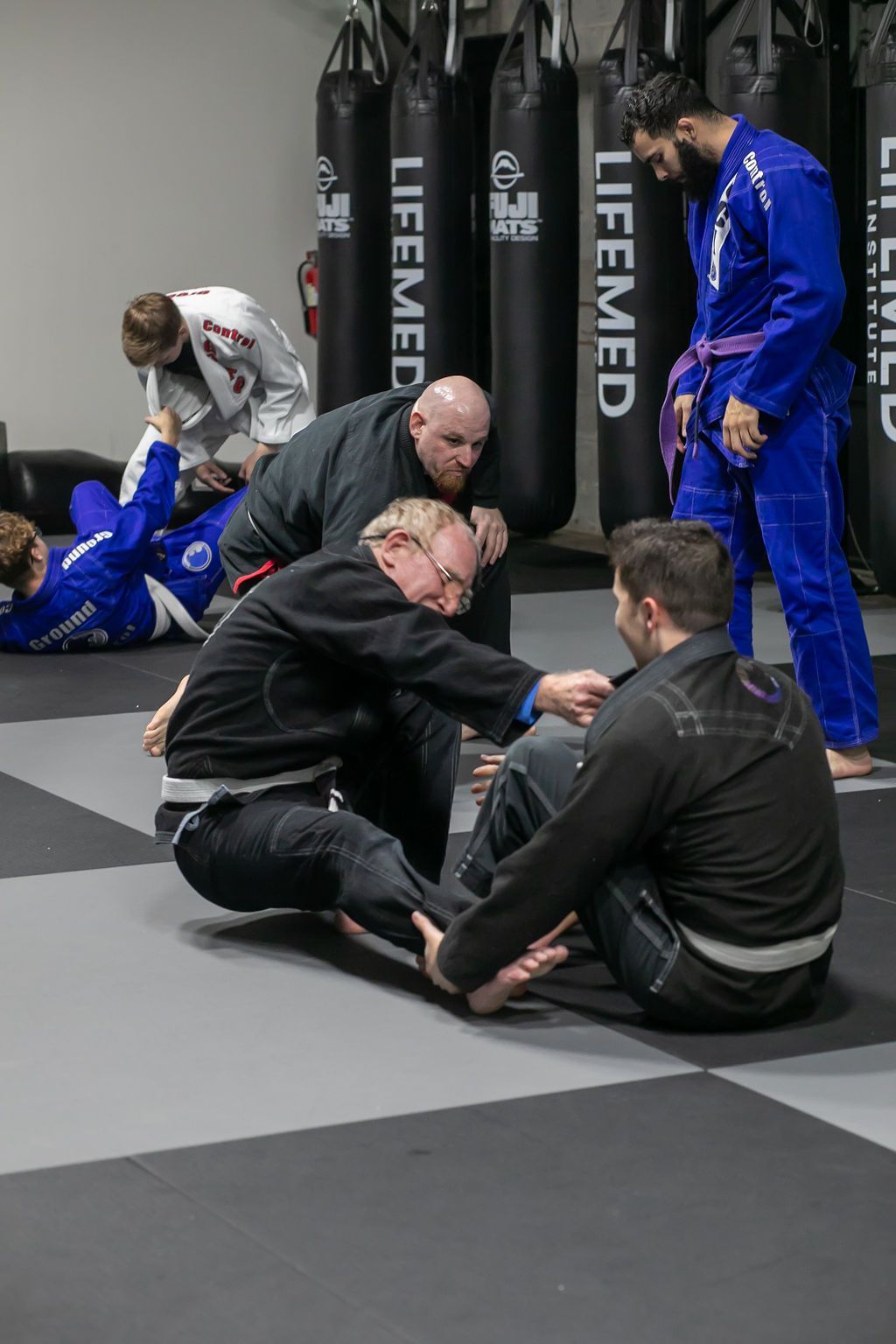 Martial arts class with students training on mats and instructors in blue uniforms in a gym