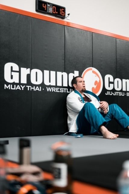 Man in blue gi rests against a black wall at a Jiu-Jitsu gym. The timer shows 4:01.