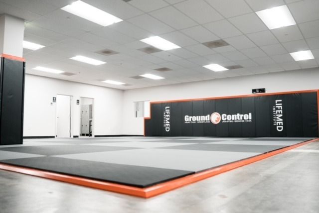 Martial arts training room with gray and orange mats, black wall padding, and bright lights.