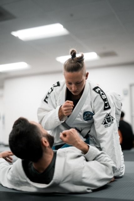 Woman in white gi over man on mat, both in a Jiu-Jitsu training session, intense focus.
