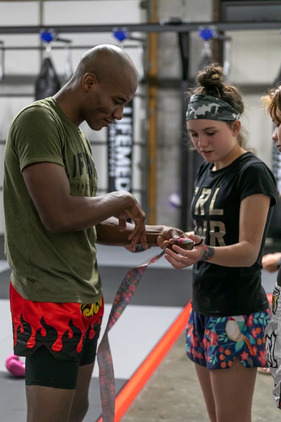 Man wrapping boxing tape on a woman's hand in a gym. Both are standing, with a focused expression.