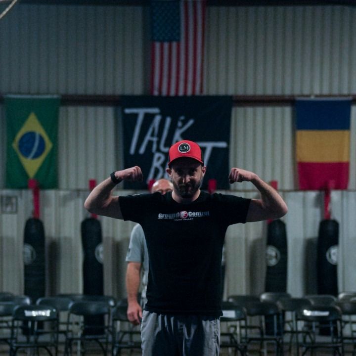 Person in a red cap flexing in a gym, with flags and a “TAL…” banner in the background