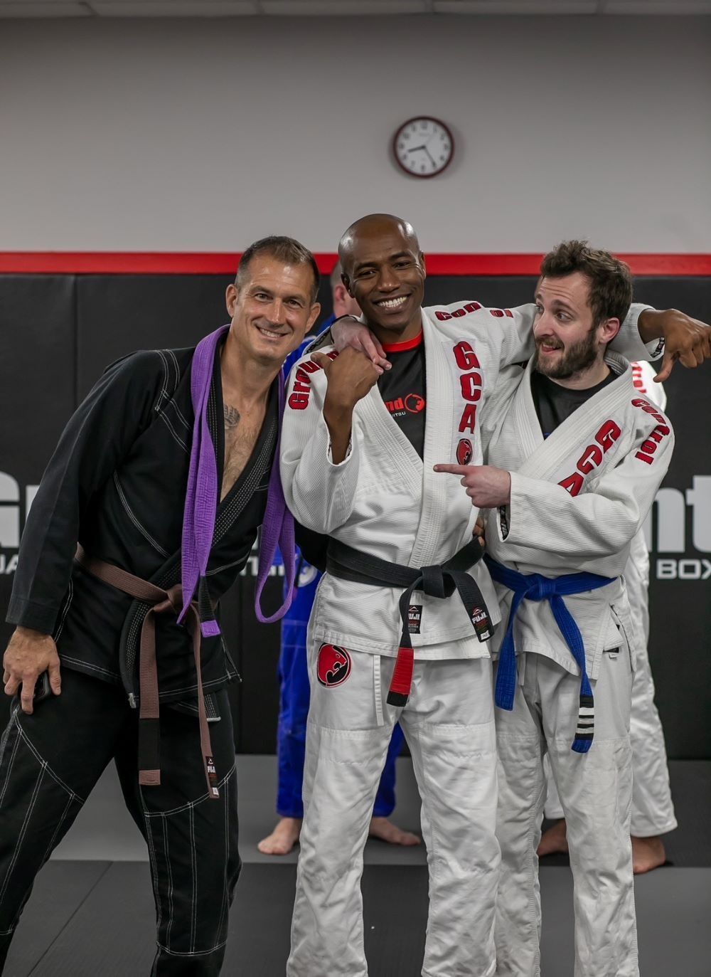 Three men in martial arts uniforms, smiling, posing in a gym.