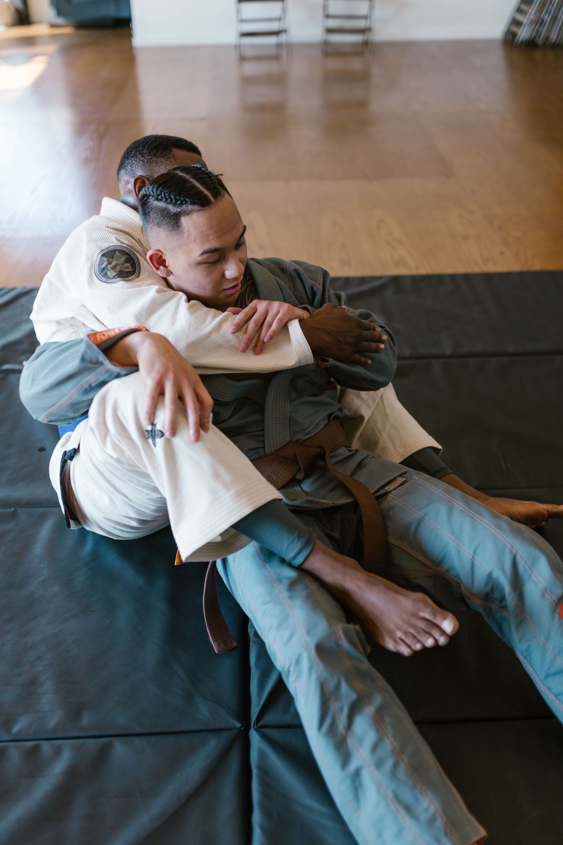 Two martial artists grappling on mats in a dojo, with two others blurred in the background.