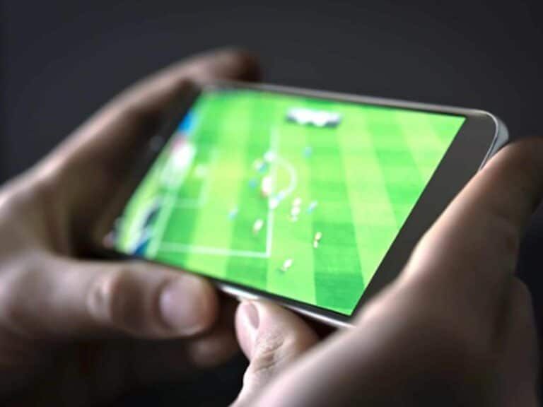 Hands holding a smartphone displaying a live broadcast of a soccer match on a green field.