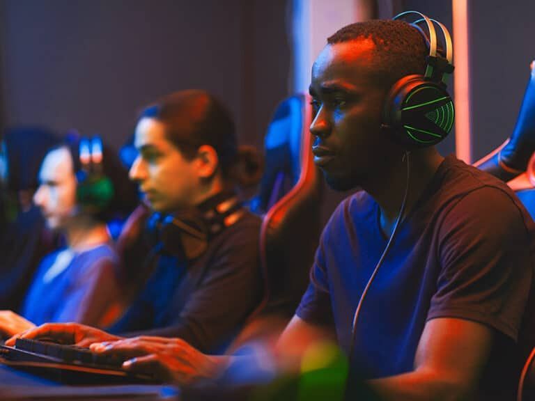 Three people with headphones focused on gaming in a dim, neon-lit room.