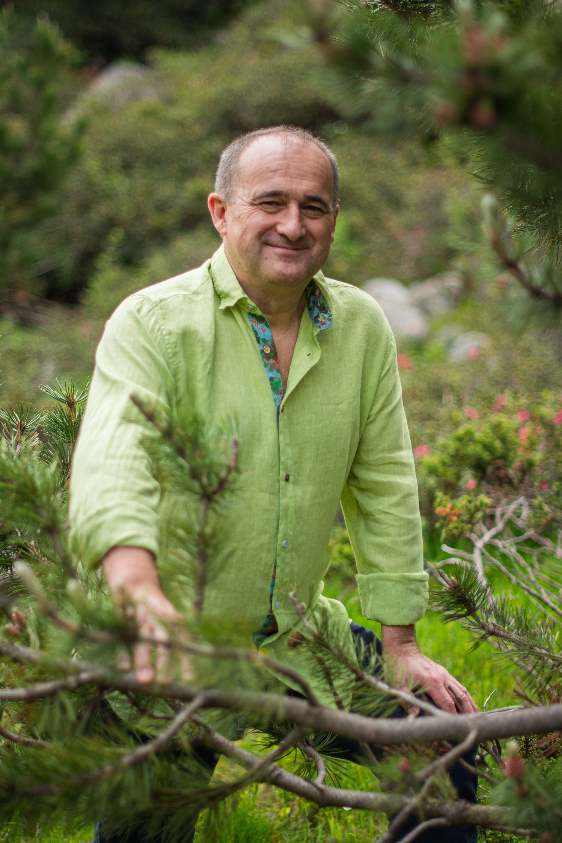 Un hombre con una camisa verde está de pie junto a la rama de un árbol.