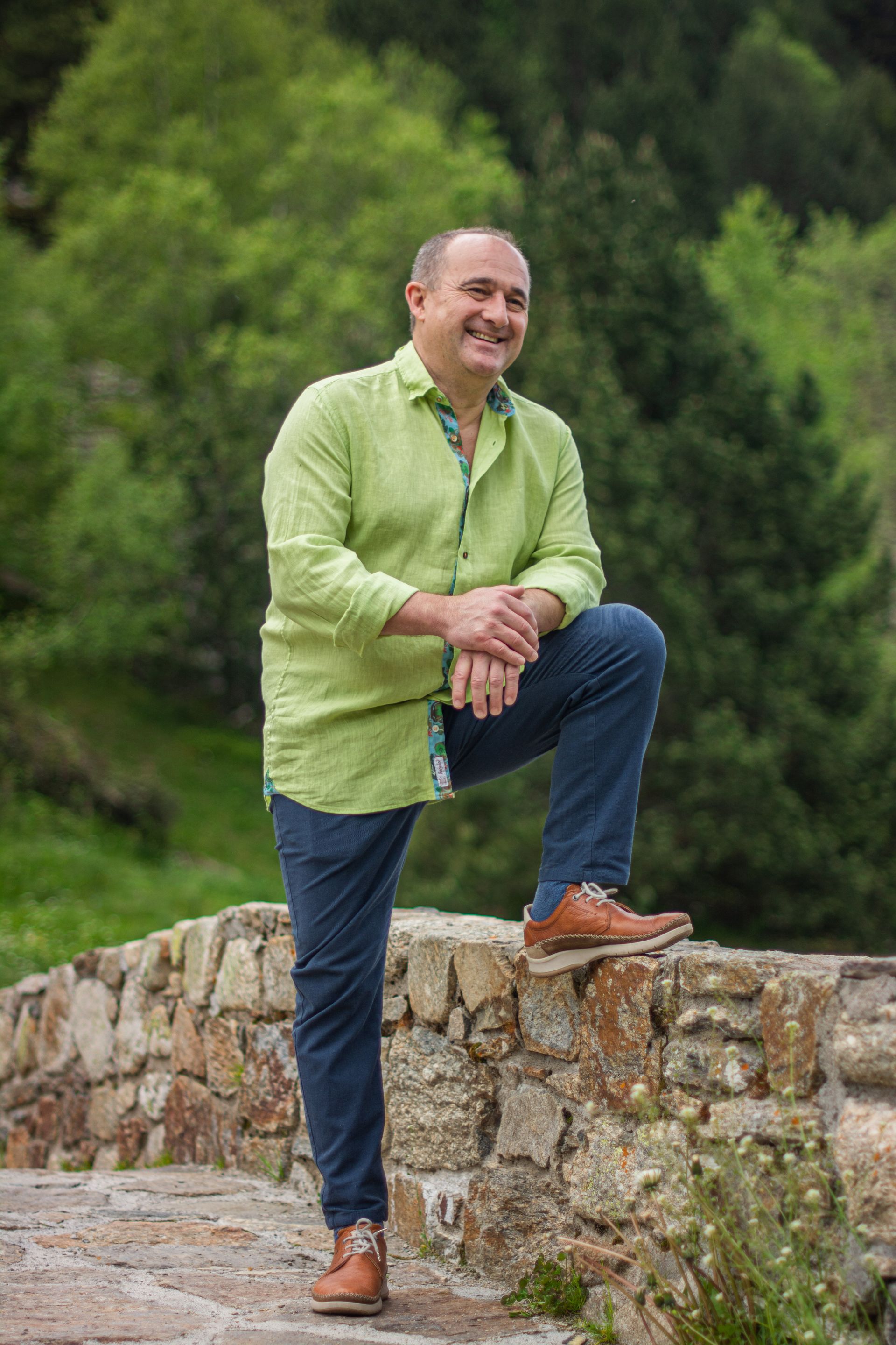 Un hombre con una camisa verde está arrodillado sobre un muro de piedra.