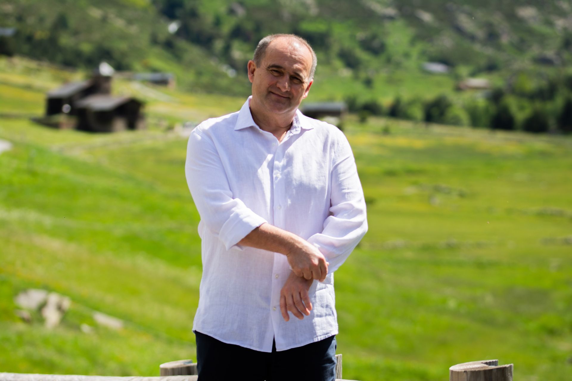 Un hombre con una camisa blanca está de pie junto a una valla de madera en un campo.