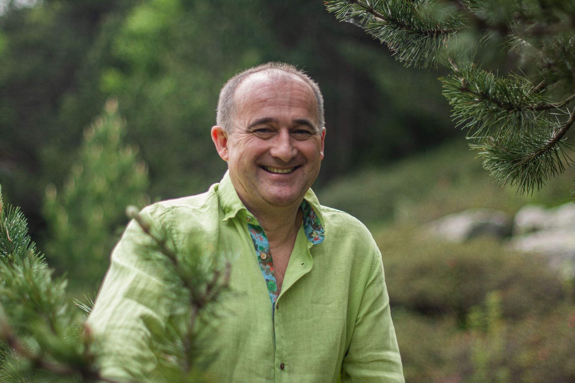 Un hombre con una camisa verde sonríe en el bosque.