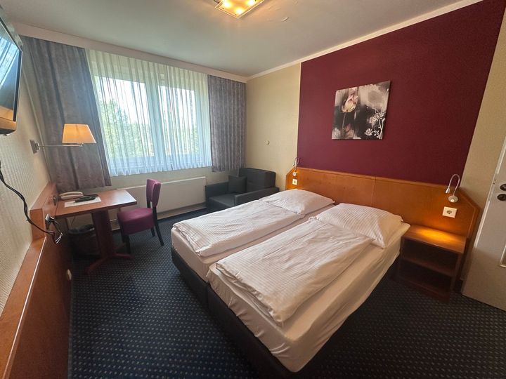 Ein Hotelzimmer mit zwei Betten, einem Stuhl, einem Schreibtisch und einem Fernseher.