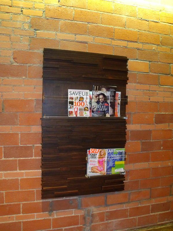 A brick wall with a wooden shelf with magazines on it