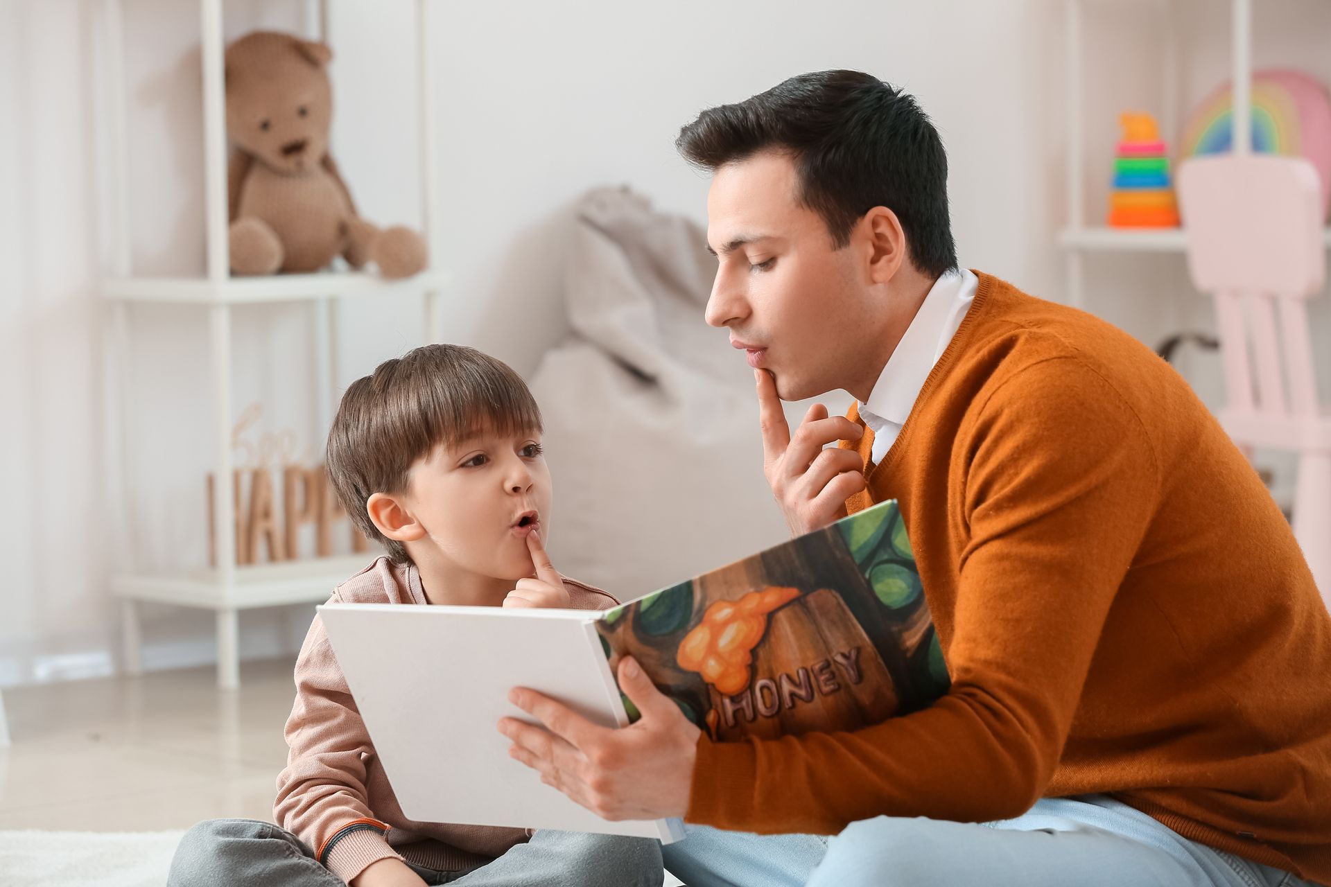 A man is sitting on the floor reading a book to his son.