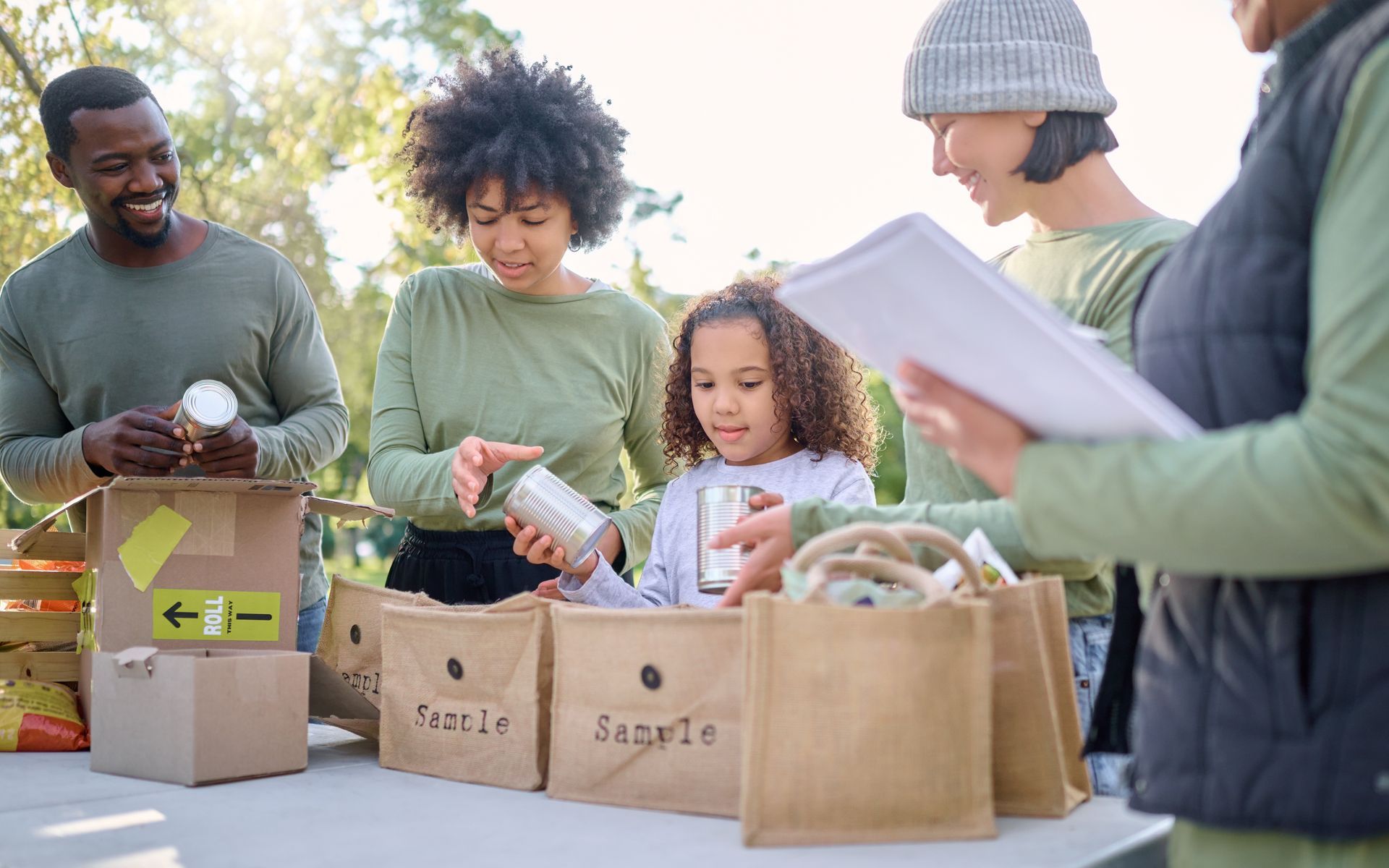A group of people are standing around a table with bags of food.