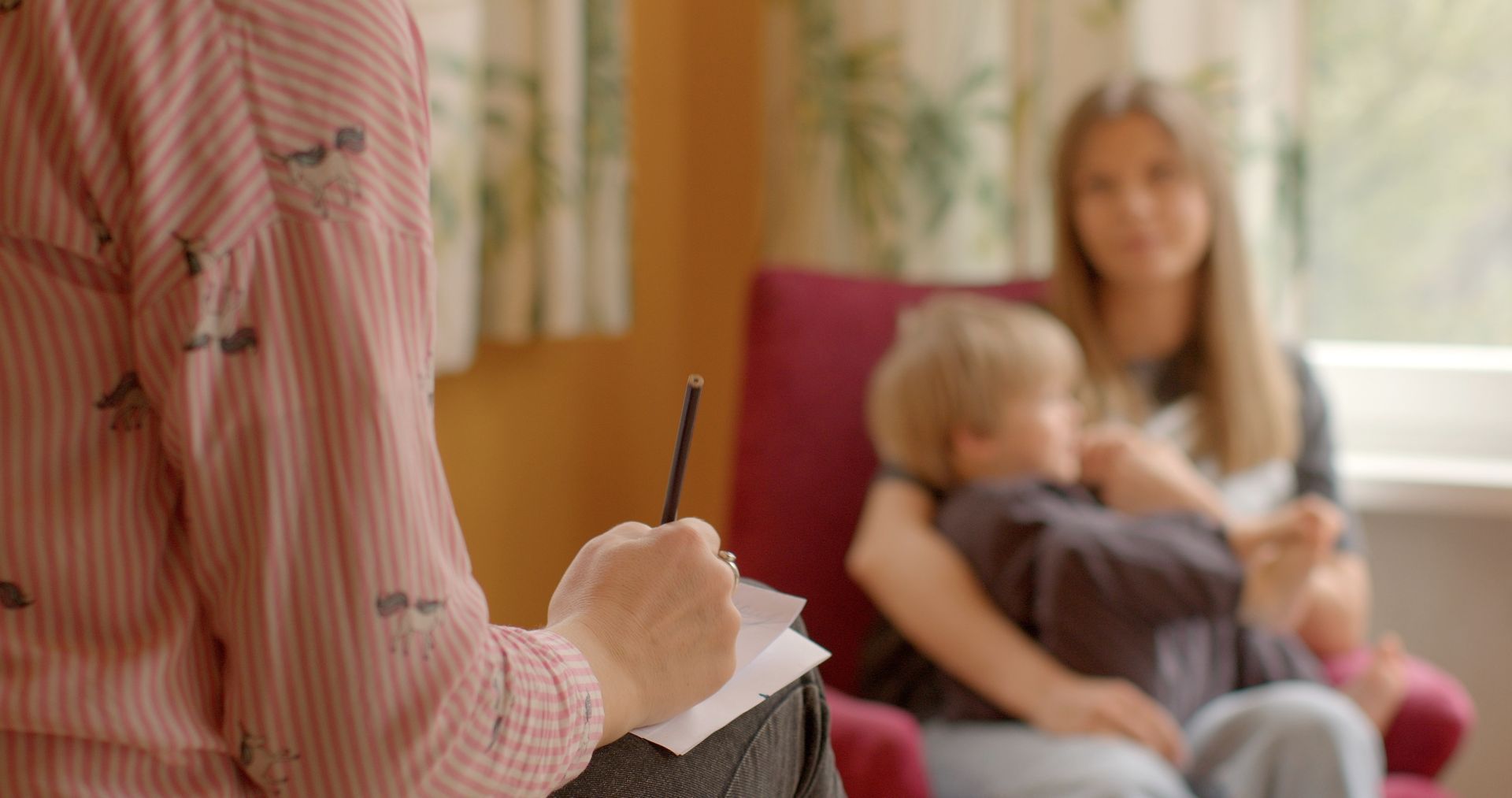 A woman is writing on a piece of paper while a woman holds a child.