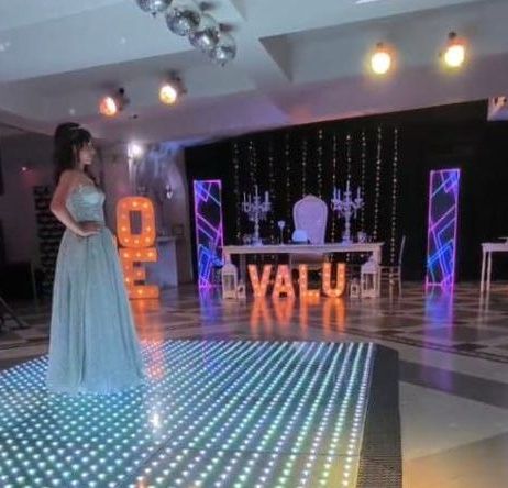 Mujer con vestido de gala posa en una pista de baile iluminada, con el letrero