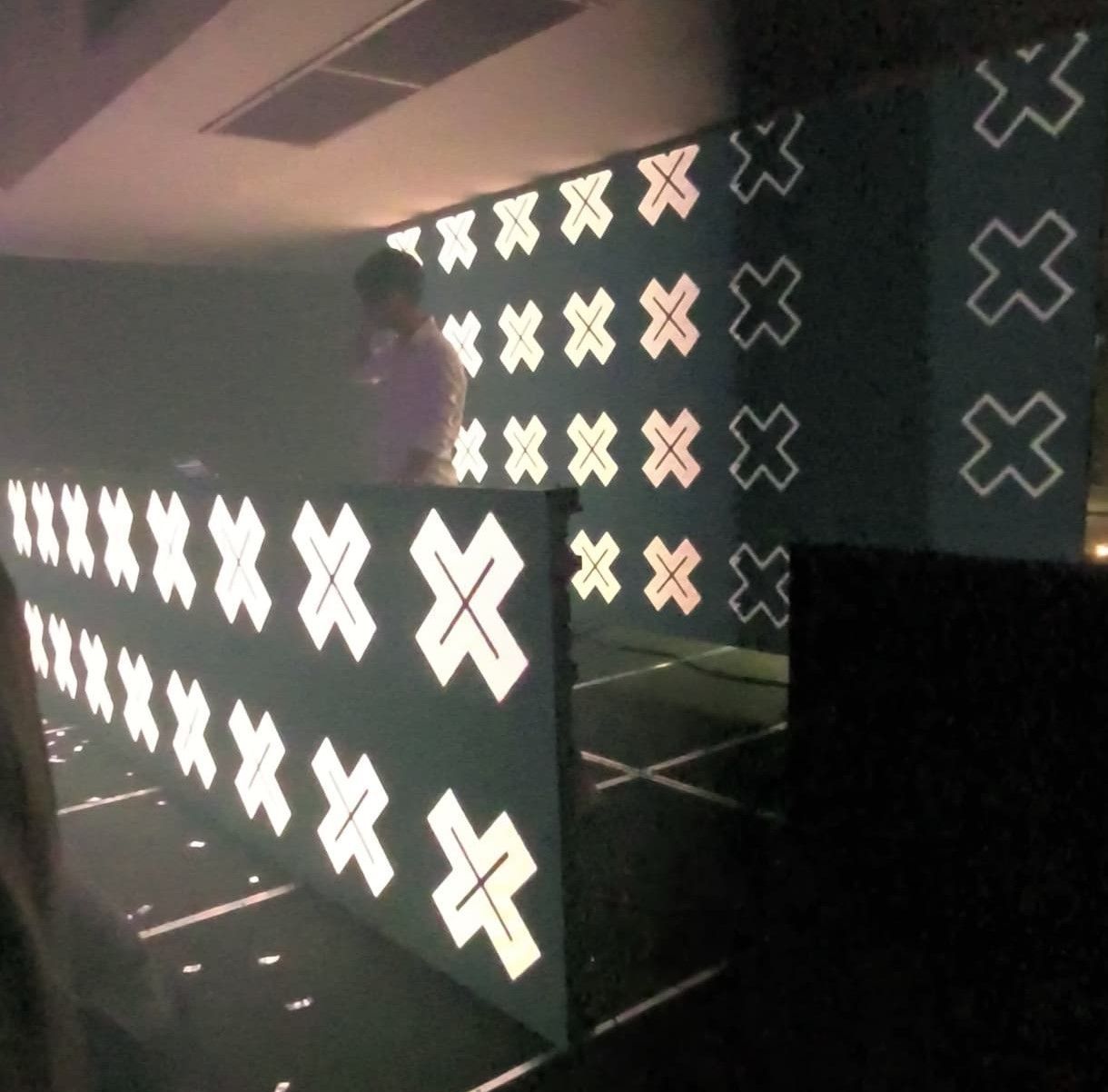 DJ de pie detrás de una cabina iluminada cubierta de formas de