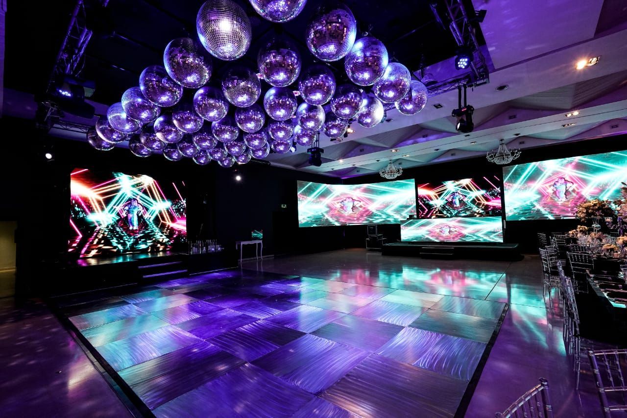 Pista de baile con paneles LED, bolas de discoteca y grandes pantallas que muestran gráficos coloridos