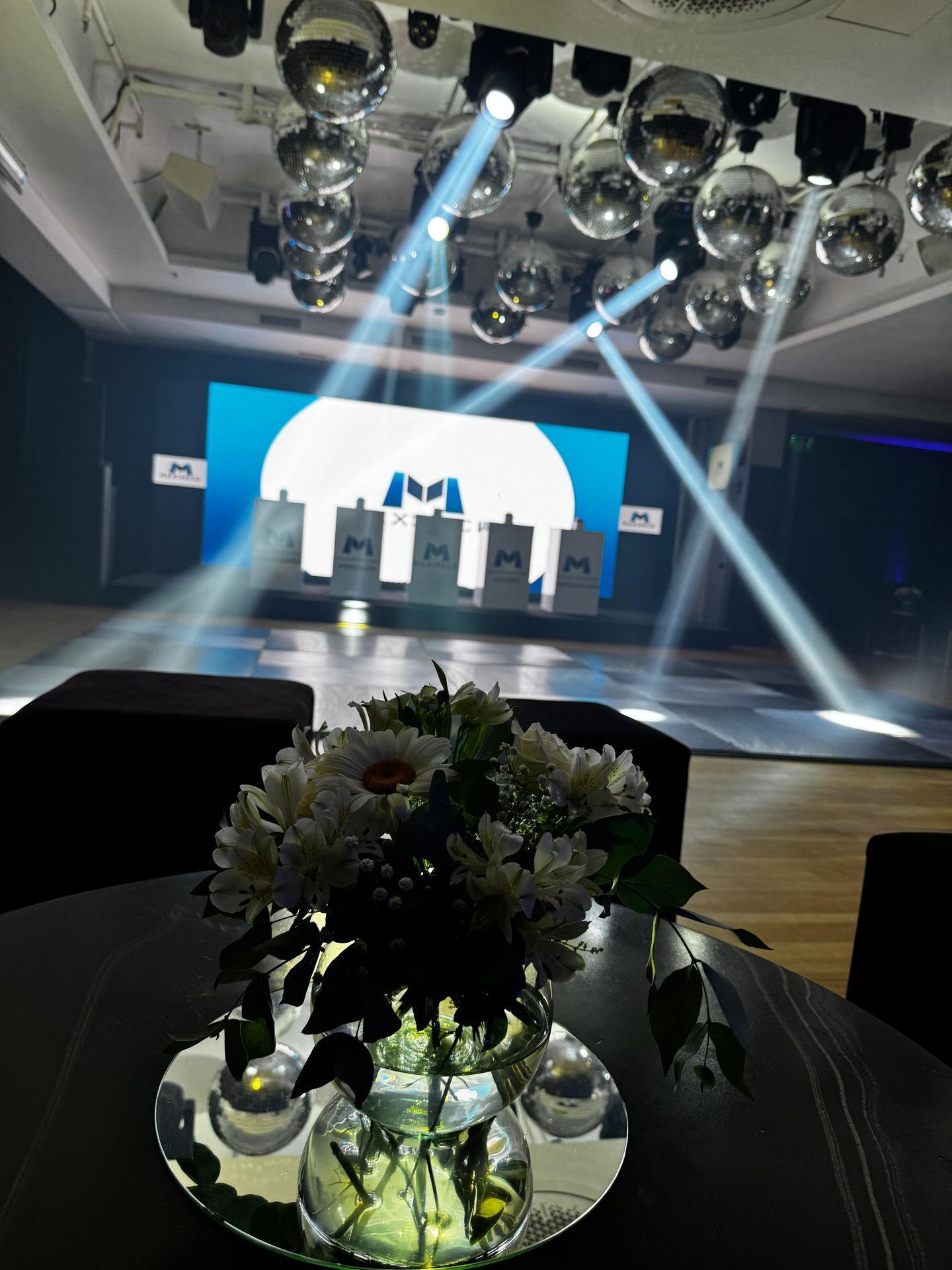 Escenario con luces brillantes, bolas de discoteca y una pantalla con un logotipo, montado para un evento.