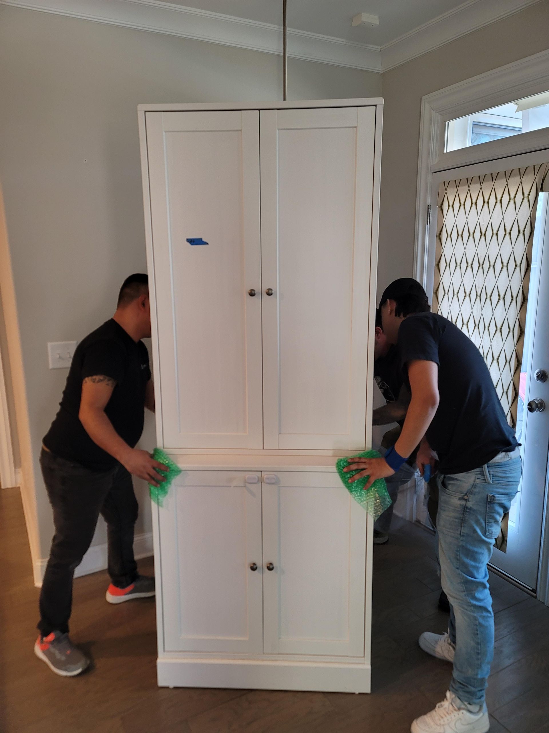 Two men are moving a large white cabinet in a room.