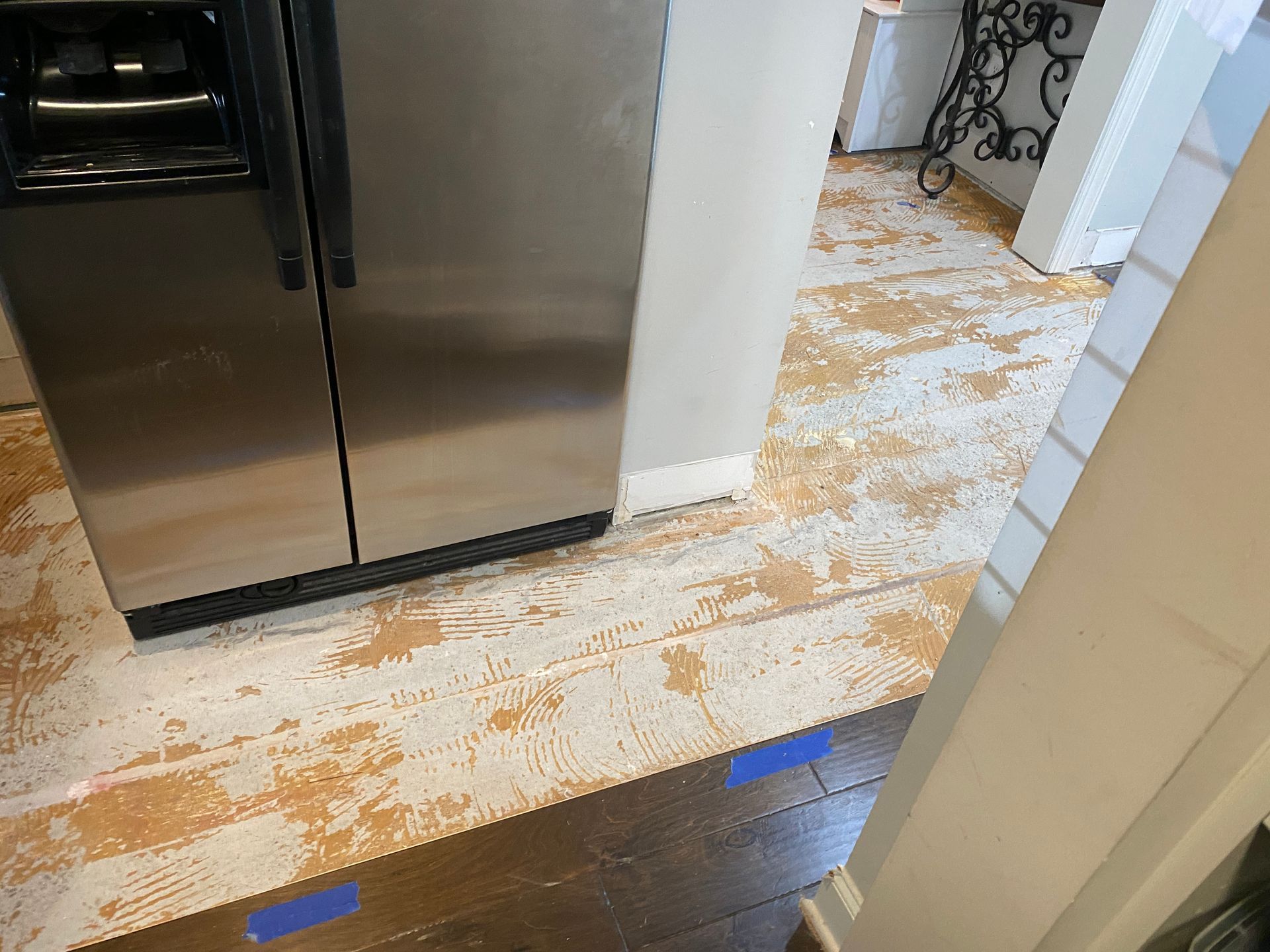 A stainless steel refrigerator is sitting next to a wooden floor in a kitchen.