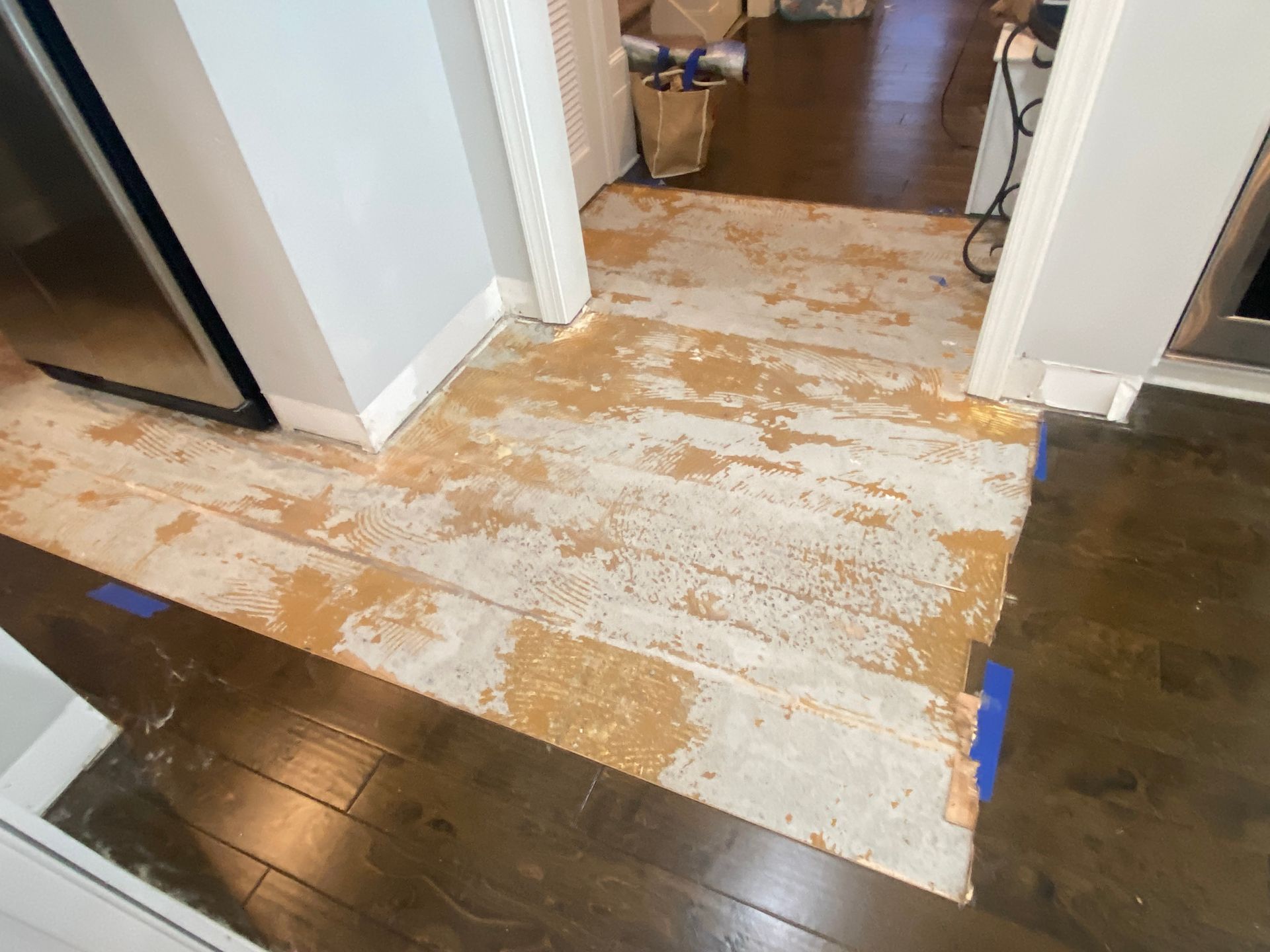 A wooden floor is being painted in a kitchen.