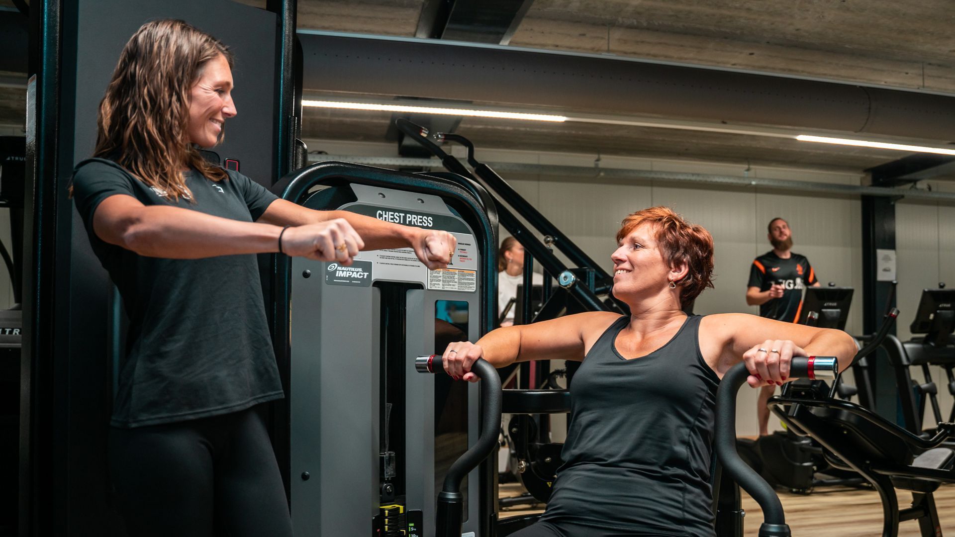 Een vrouw traint met een personal trainer in een sportschool. Beiden glimlachen.