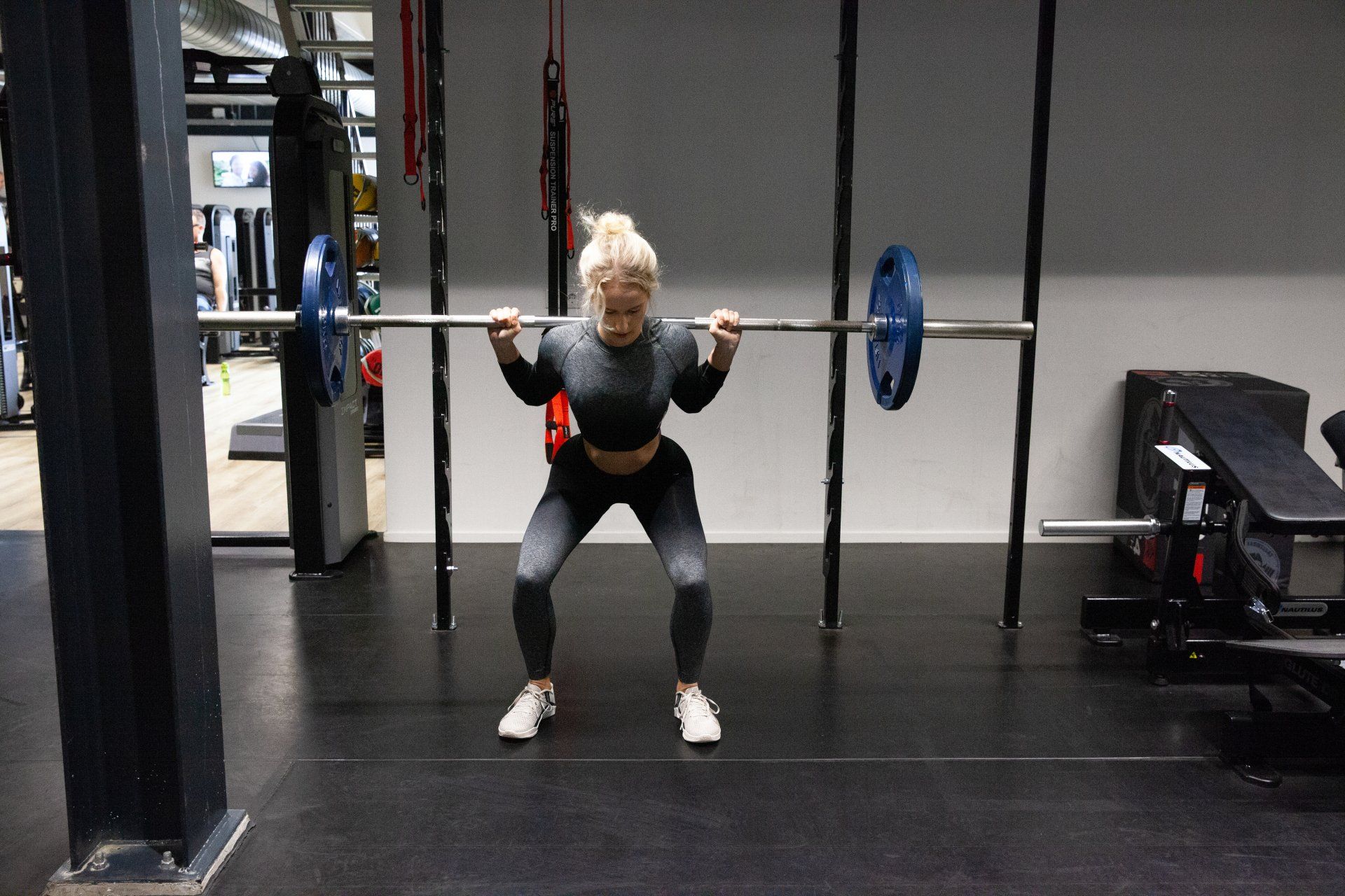 Een vrouw voert een squat met een halter uit in een sportschool. Ze draagt ​​sportkleding.