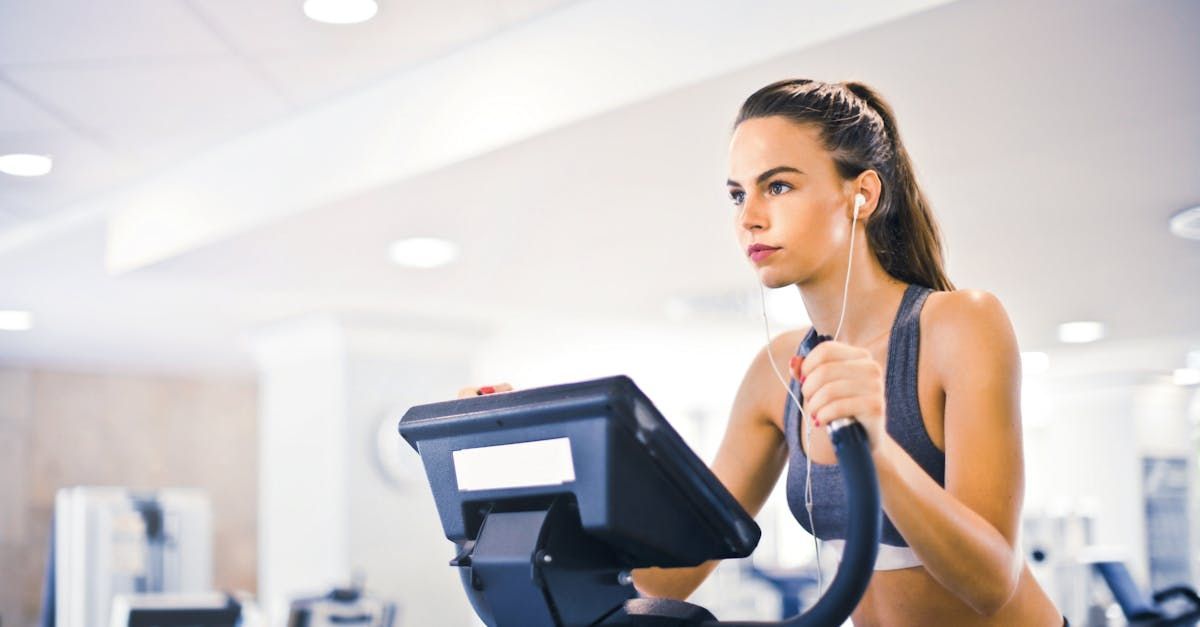 Een vrouw traint op een crosstrainer in een sportschool, terwijl ze een sportbeha draagt ​​en naar muziek luistert.