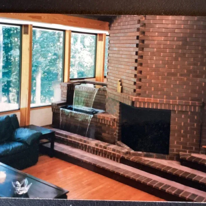 A large, multi-tiered brick fireplace with an integrated waterfall feature in a room with floor-to-ceiling windows.