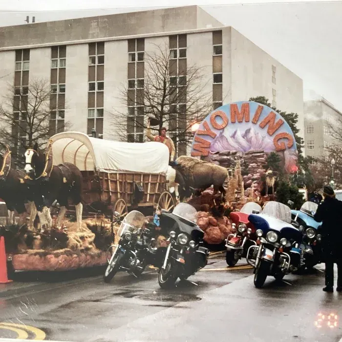 A Wyoming state parade float featuring a covered wagon and a bison sculpture, accompanied by police motorcycles.
