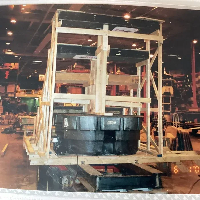 A large, black industrial tank inside a wooden shipping crate in a warehouse setting.