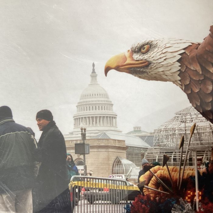 A large eagle statue stands before the U.S. Capitol building, with people walking in the foreground on a snowy day.