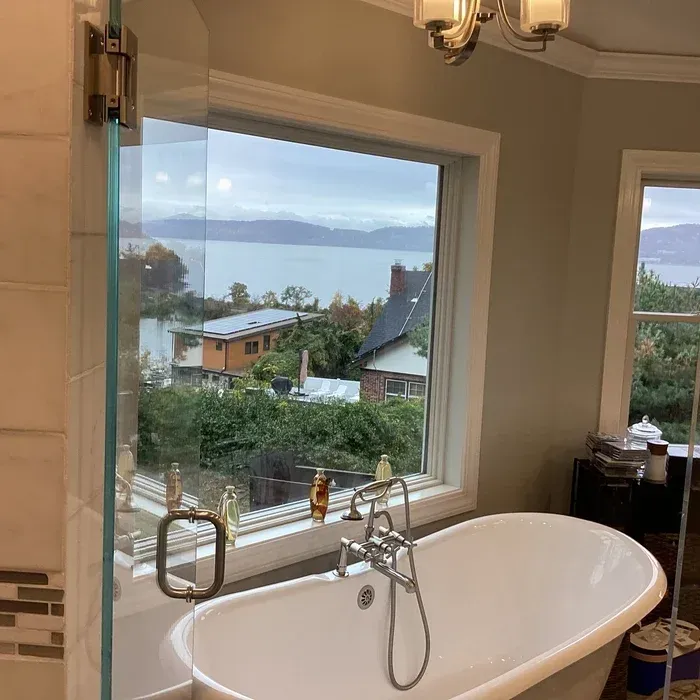 A white freestanding bathtub set against a large window with a scenic view of a lake, hills, and nearby houses.