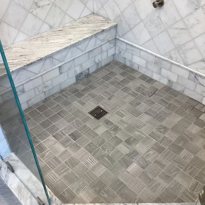 A modern shower with light gray marble walls, a textured gray tiled floor, and a stone bench.