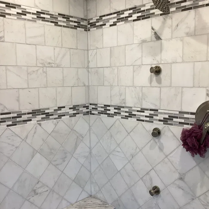 A marble-tiled shower wall features square and diamond patterns separated by horizontal strips of gray and white mosaic.