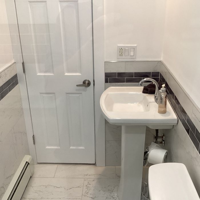 A white pedestal sink with a metal faucet stands in a bathroom next to a closed white door and tiled walls.