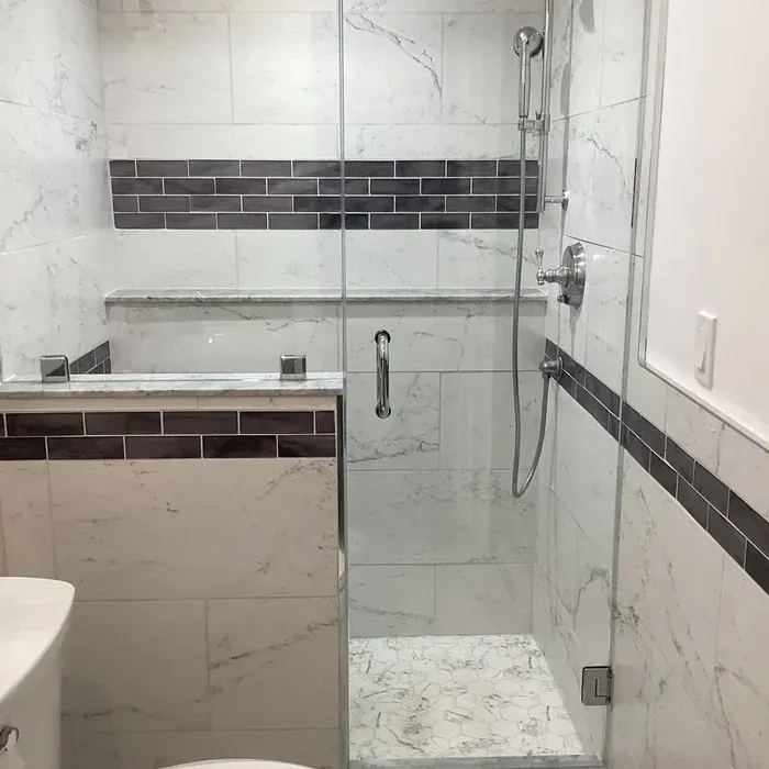 A modern shower with white marble-patterned tiles, a dark horizontal accent stripe, and a clear glass enclosure.