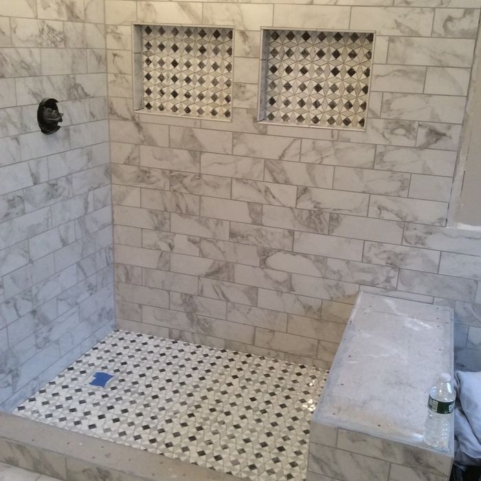 A modern shower with white marble-look subway wall tiles, a matching mosaic tile floor, two recessed niches, and a bench.