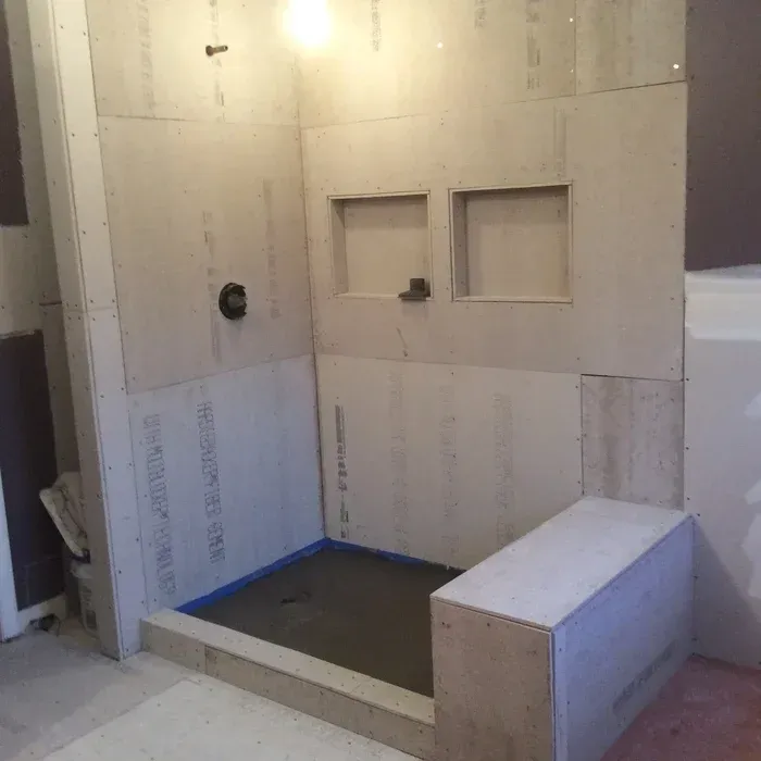 A partially constructed walk-in shower with cement board walls, a built-in bench, two niches, and a waterproofed base.