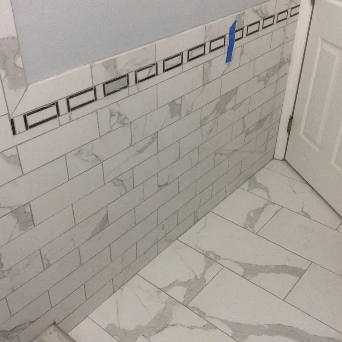 White marble-style subway tiles on a wall with a decorative black and white border, meeting a matching tiled floor.
