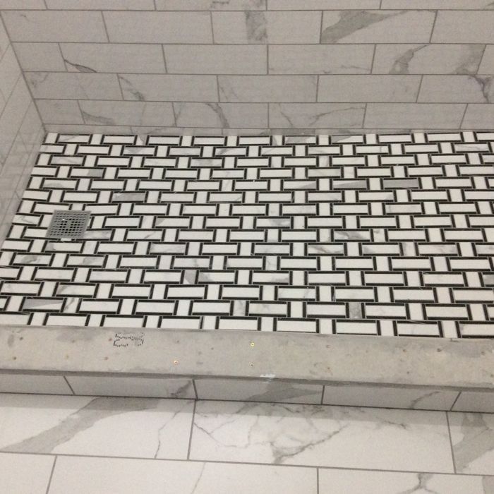 A walk-in shower with a black-and-white basketweave tile floor and white marble-look subway tile walls.